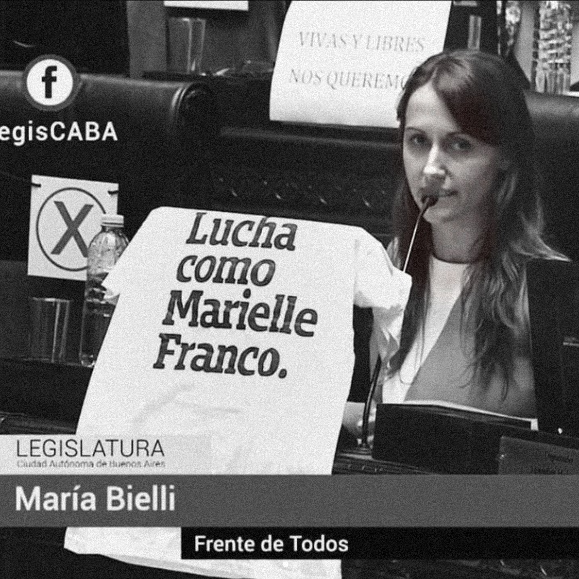 Foto preta e branca de uma mulher branca, de cabelos castanhos, lisos e médios. Em cima do monitor tem uma camiseta branca escrita lucha como Marielle Franco em preto.