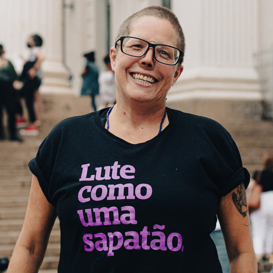 card branco escrito PRÉ-VENDA e imagem do mockup de uma camiseta preta com a frase lute como uma sapatão em roxo. 