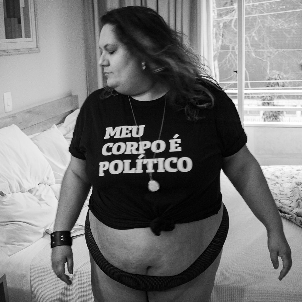 foto preto e branco de um umbigo aparecendo entre a camiseta e calça. Na camiseta preta está escrito gorda em branco. 