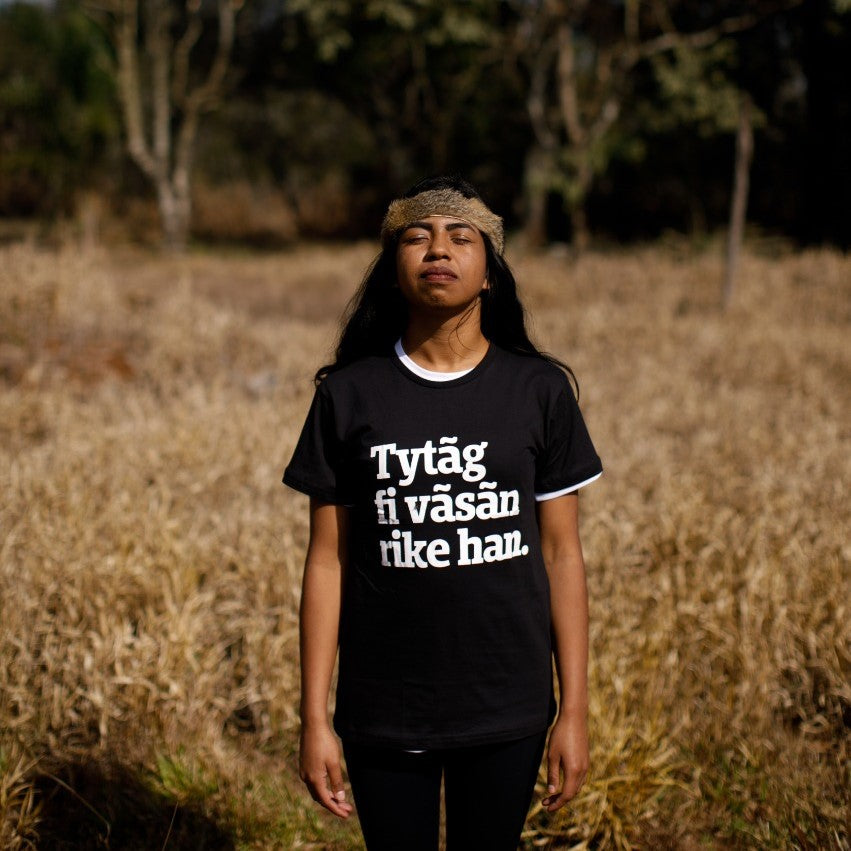 foto mulher indígena com cabelos preto, compridos, com camiseta peita com a frase lute como uma garota no idioma kaingang