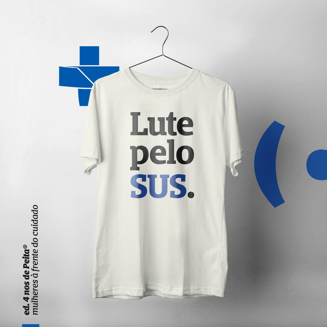 Foto colorida de uma camiseta branca com a frase lute pelo sus em preto, sendo que a palavra sus está em azul. o fundo é uma arte com a logo do sus, da peita e escrito: ed. 4 anos de peita. mulheres à frente do cuidado. 